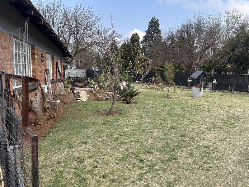 A spacious rear garden featuring a brick exterior facade, a decorative well, and a lawn area with established landscaping and perimeter fencing.