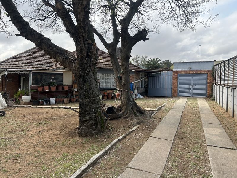 Rear view of the property featuring a brick facade, tiled roof, concrete driveway, and a detached garage structure with a metal door.