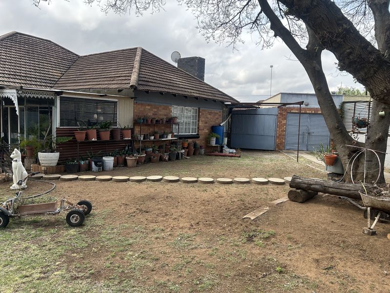 Rear view of the property featuring a brick facade, tiled roof, and a large garden area with established trees and garage access.