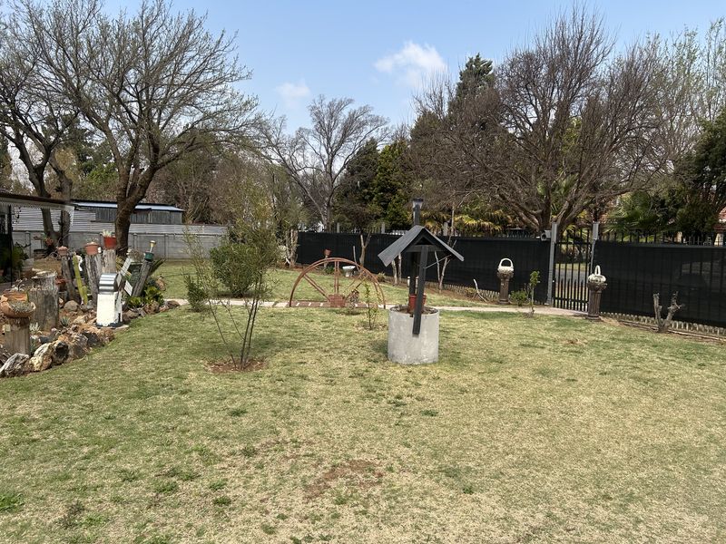 A spacious residential garden featuring a well-maintained lawn, perimeter fencing, and a decorative well feature.