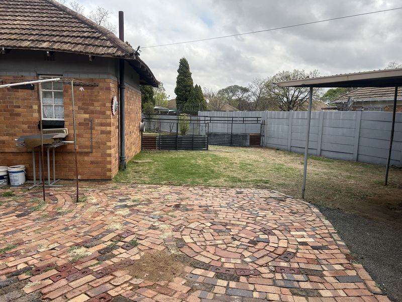 Rear garden area featuring a brick-paved patio, a metal carport structure, and perimeter precast concrete walling.