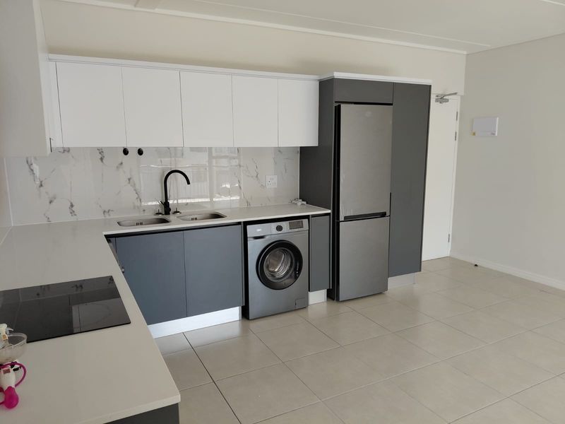 Modern kitchen featuring sleek grey and white cabinetry, marble-look splashback, integrated appliances, and neutral tiled flooring in an open-plan layout.