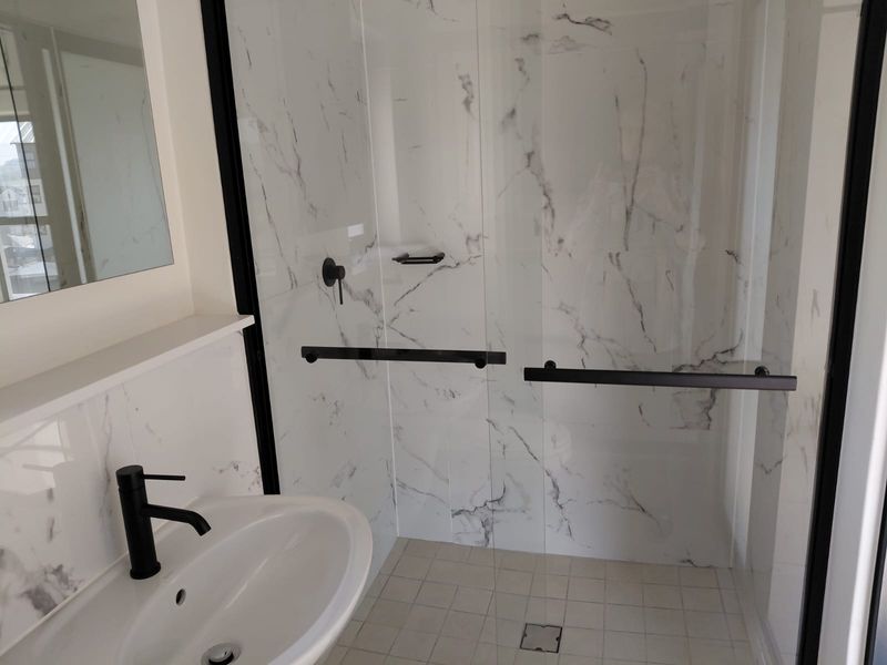Modern bathroom featuring a walk-in shower with marble-look wall tiles, black matte fixtures, and a sleek pedestal basin.