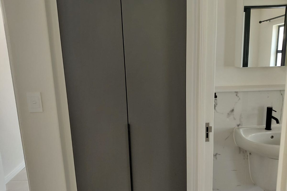 A modern bathroom featuring a pedestal washbasin with a black mixer tap, marble-look wall tiles, and a built-in storage cupboard.