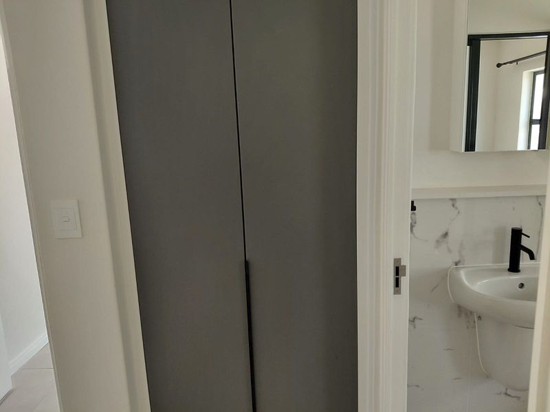 A modern bathroom featuring a pedestal washbasin with a black mixer tap, marble-look wall tiles, and a built-in storage cupboard.