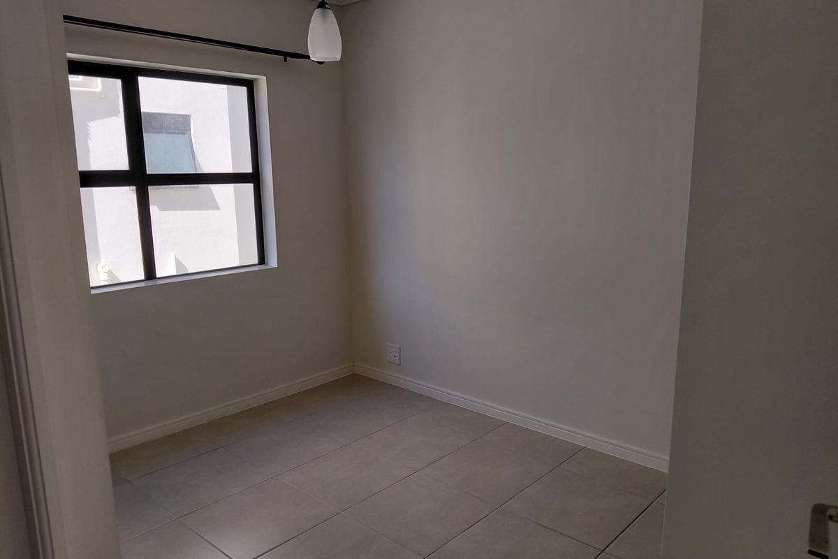 A clean, empty bedroom featuring neutral tiled flooring, a modern aluminium window, and a simple pendant light fixture.
