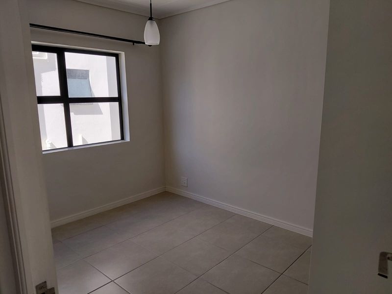 A clean, empty bedroom featuring neutral tiled flooring, a modern aluminium window, and a simple pendant light fixture.