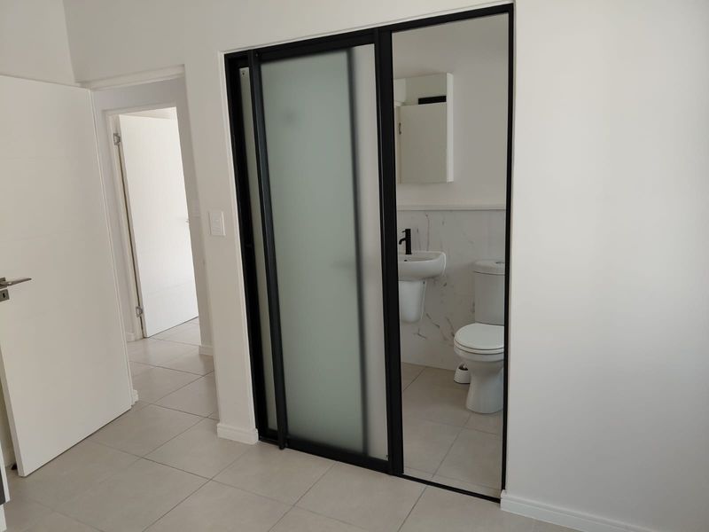 A modern bathroom featuring a sliding frosted glass door, wall-mounted basin, toilet, and elegant marble-look wall tiles.