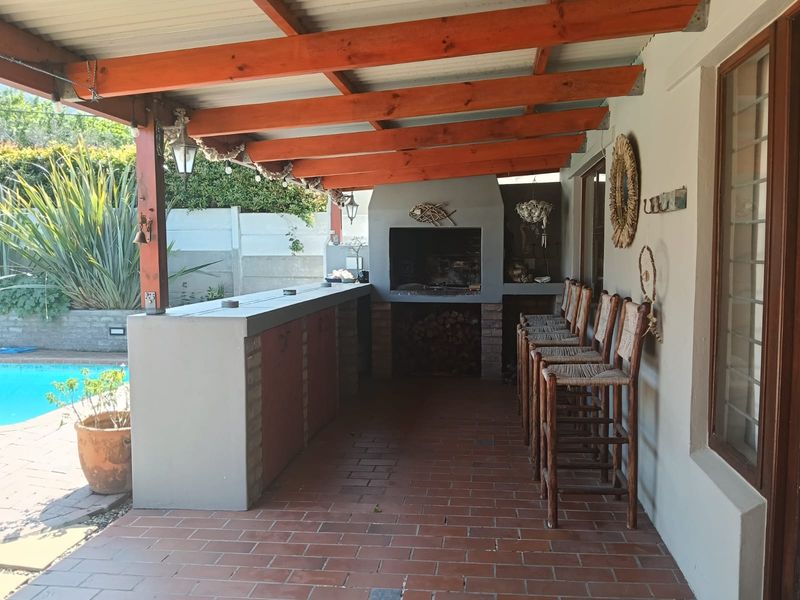 Covered outdoor patio featuring a built-in braai, bar counter, and brick flooring, overlooking a swimming pool area.