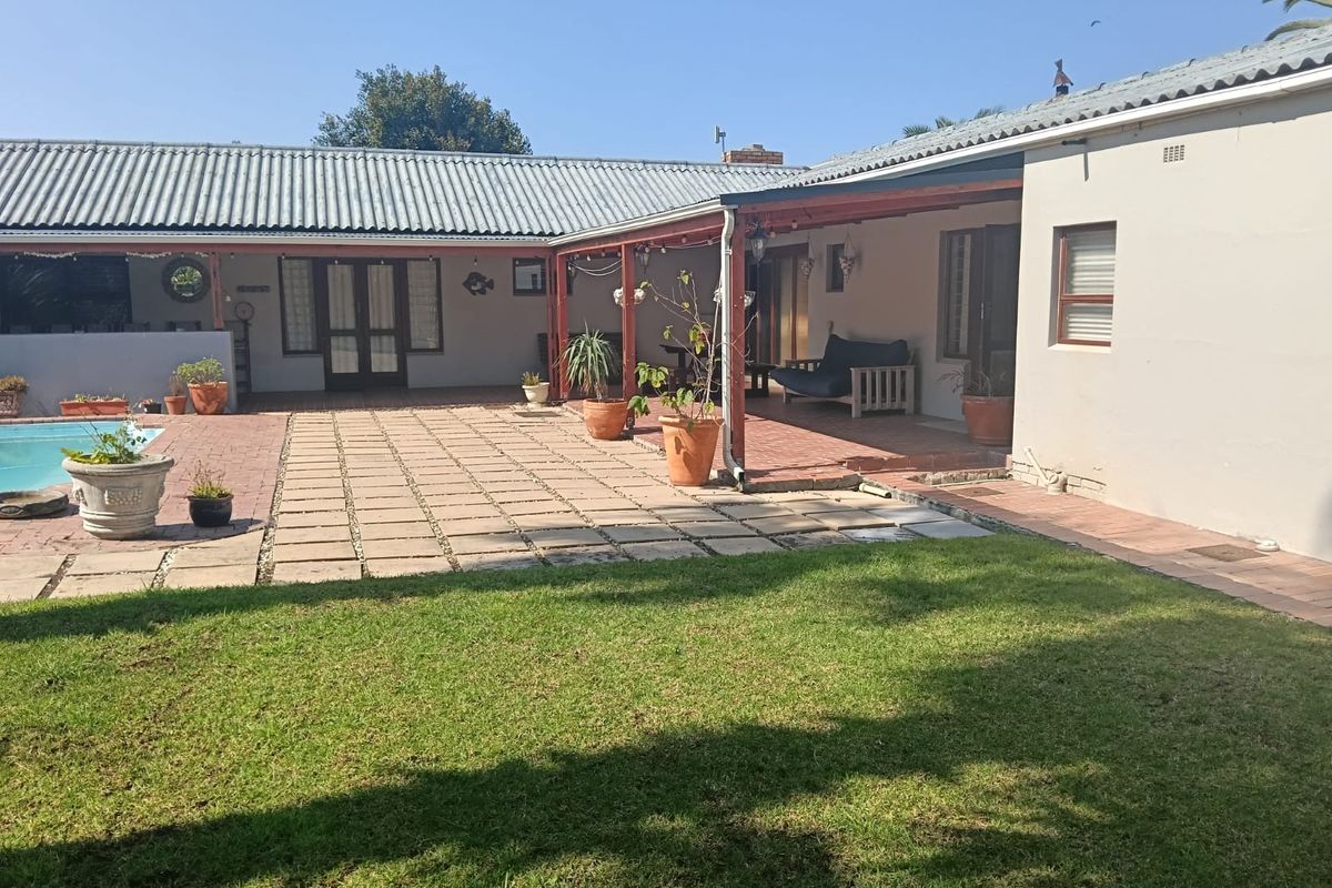 Rear exterior view featuring a paved patio area, covered veranda, and a swimming pool set within a private garden.
