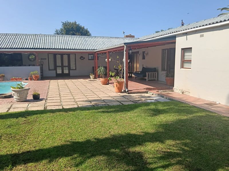 Rear exterior view featuring a paved patio area, covered veranda, and a swimming pool set within a private garden.