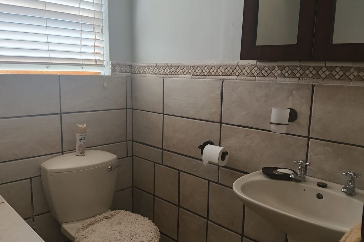 A functional bathroom featuring tiled walls, a pedestal basin, a toilet, and a wall-mounted mirror cabinet with venetian blinds for privacy.