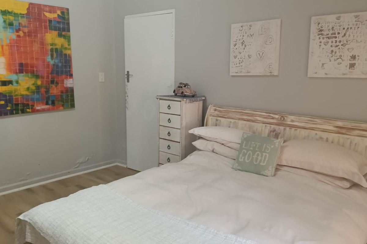 A bedroom featuring laminate flooring and neutral wall tones, showing visible signs of moisture damage on the lower wall section.