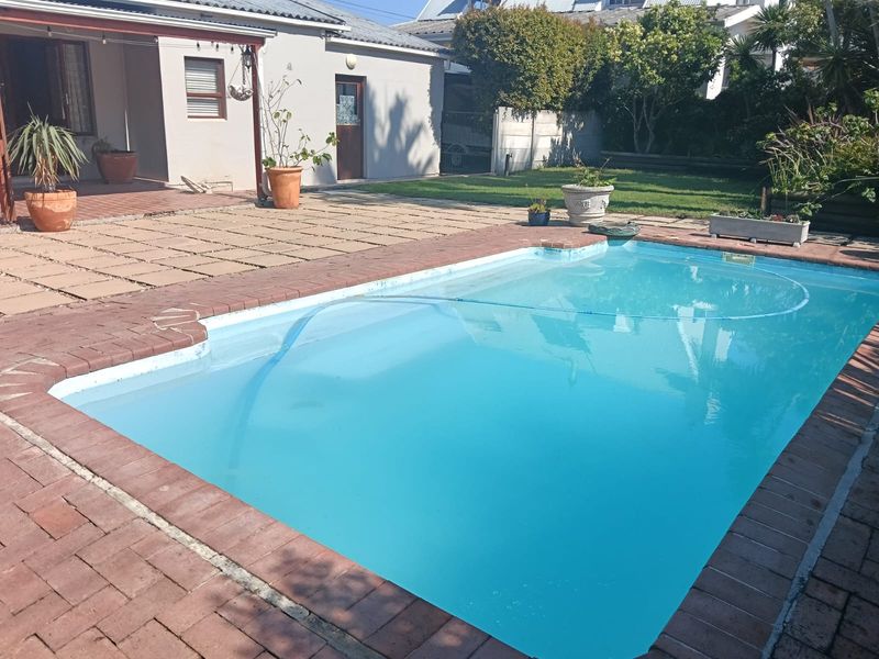 Outdoor pool area featuring a swimming pool with brick paving surround, adjacent to a covered patio and a rear garden space.