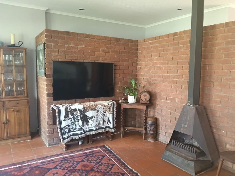 Living room featuring an exposed brick wall, terracotta floor tiles, and a freestanding metal fireplace.