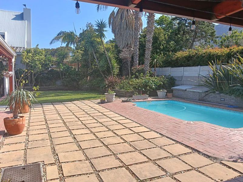 Outdoor pool area featuring a paved patio, swimming pool, and established garden with a boundary wall.