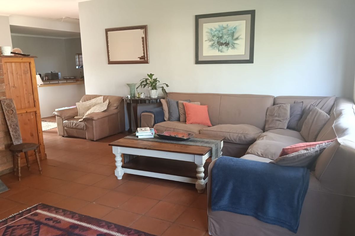 A spacious living room featuring terracotta floor tiles and a brick fireplace, with an open-plan layout leading towards the kitchen area.