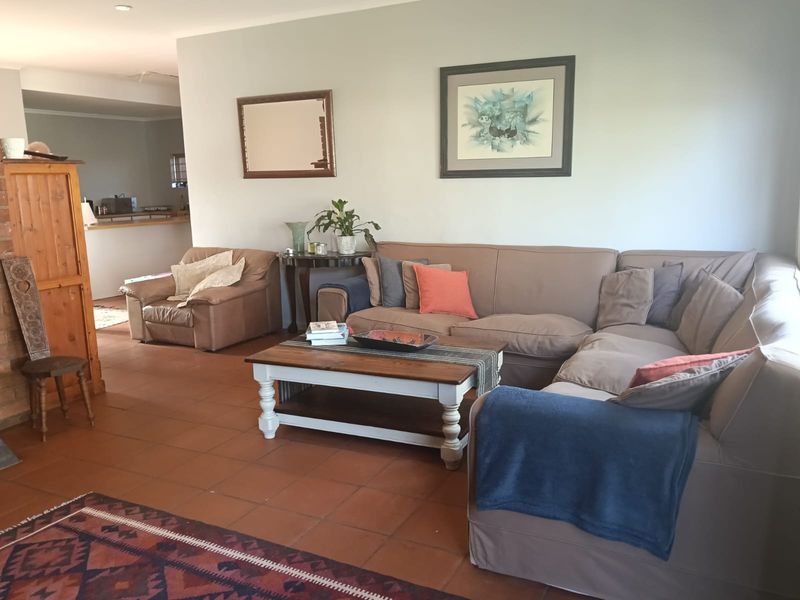 A spacious living room featuring terracotta floor tiles and a brick fireplace, with an open-plan layout leading towards the kitchen area.