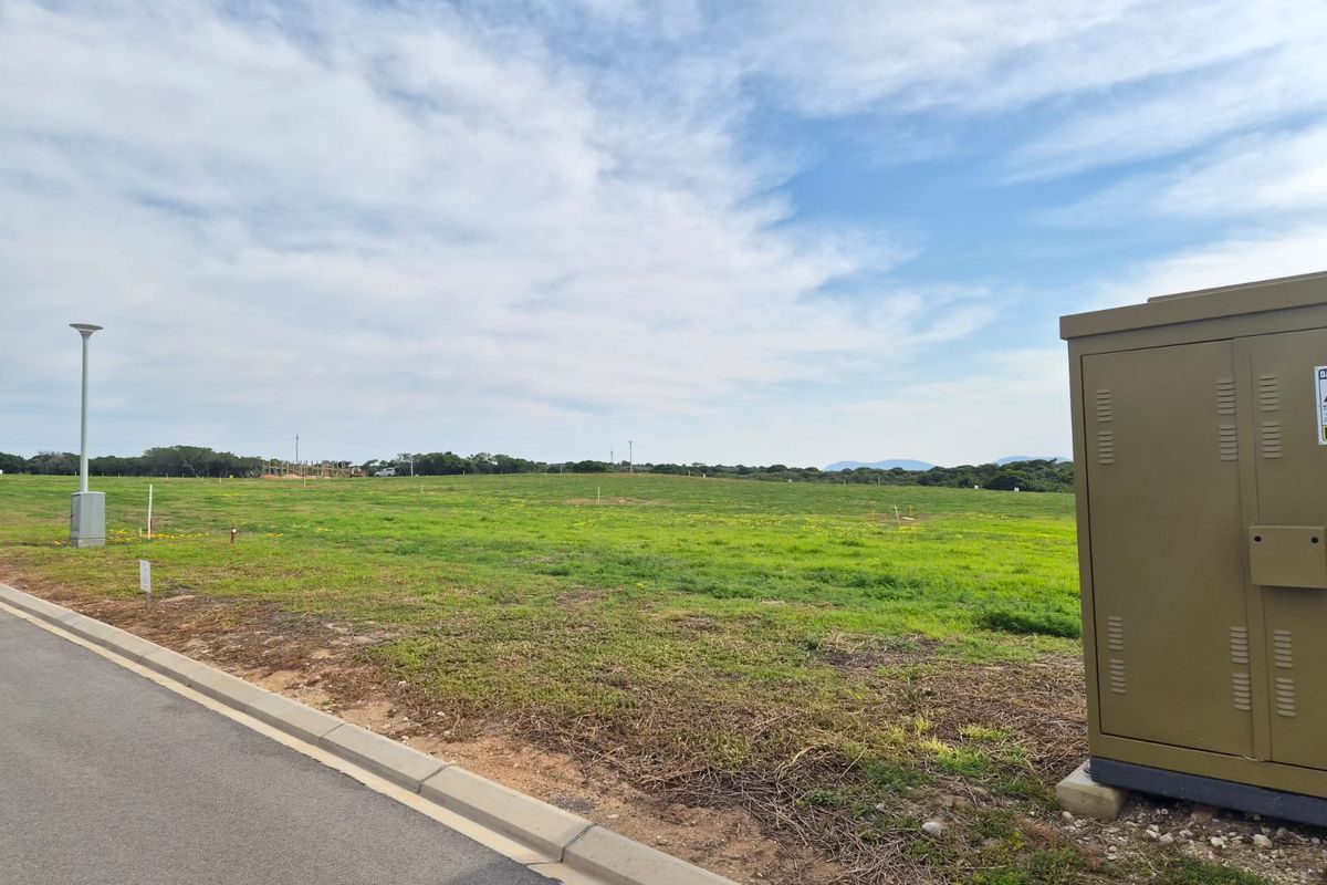 A view of a vacant residential plot featuring a grassy landscape, paved curb, and existing electrical utility infrastructure.