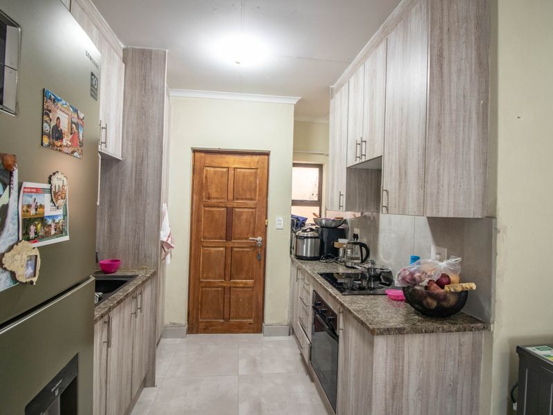 A functional galley-style kitchen featuring light wood-grain cabinetry, granite countertops, integrated oven and hob, and tiled flooring.