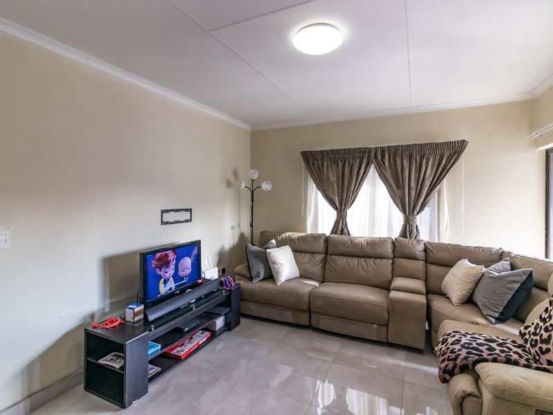 A comfortable living room featuring neutral wall tones, large format floor tiles, and a coved ceiling with a central light fixture.