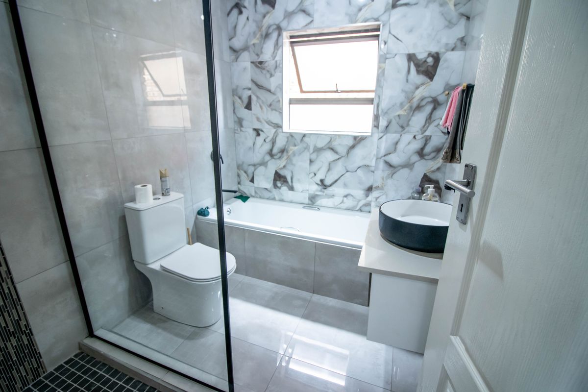Modern bathroom featuring a bathtub, vessel sink vanity, toilet, and glass shower screen with contemporary marble-effect wall tiling.
