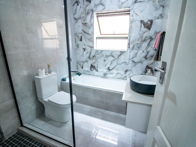 Modern bathroom featuring a bathtub, vessel sink vanity, toilet, and glass shower screen with contemporary marble-effect wall tiling.