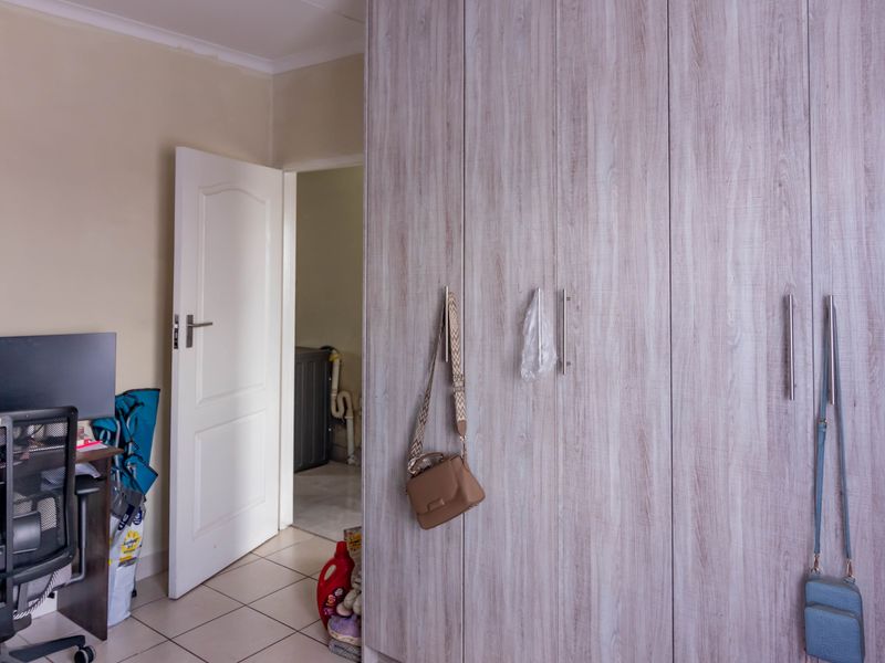 A bedroom featuring light wood-grain built-in cupboards and tiled flooring, with an open doorway leading to an adjacent utility area.
