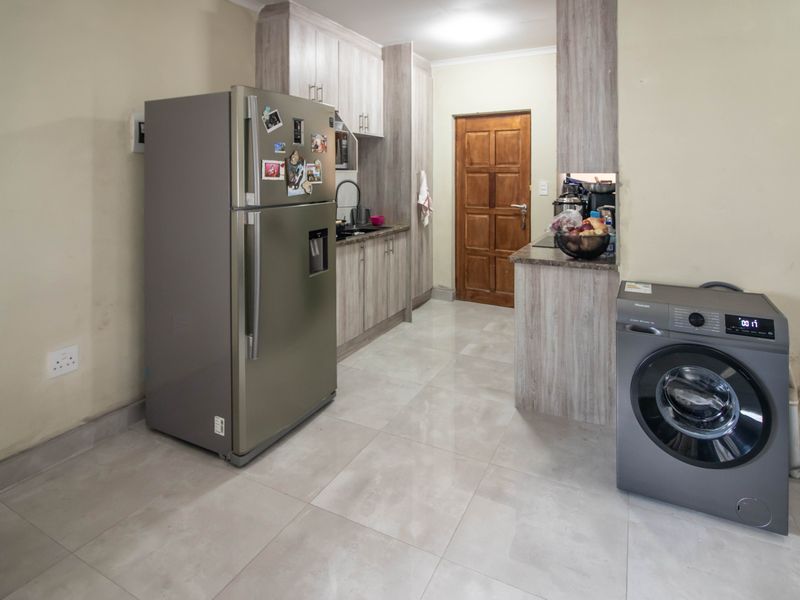 A functional kitchen featuring light wood-look cabinetry, tiled flooring, and a wooden door leading to an adjacent area.