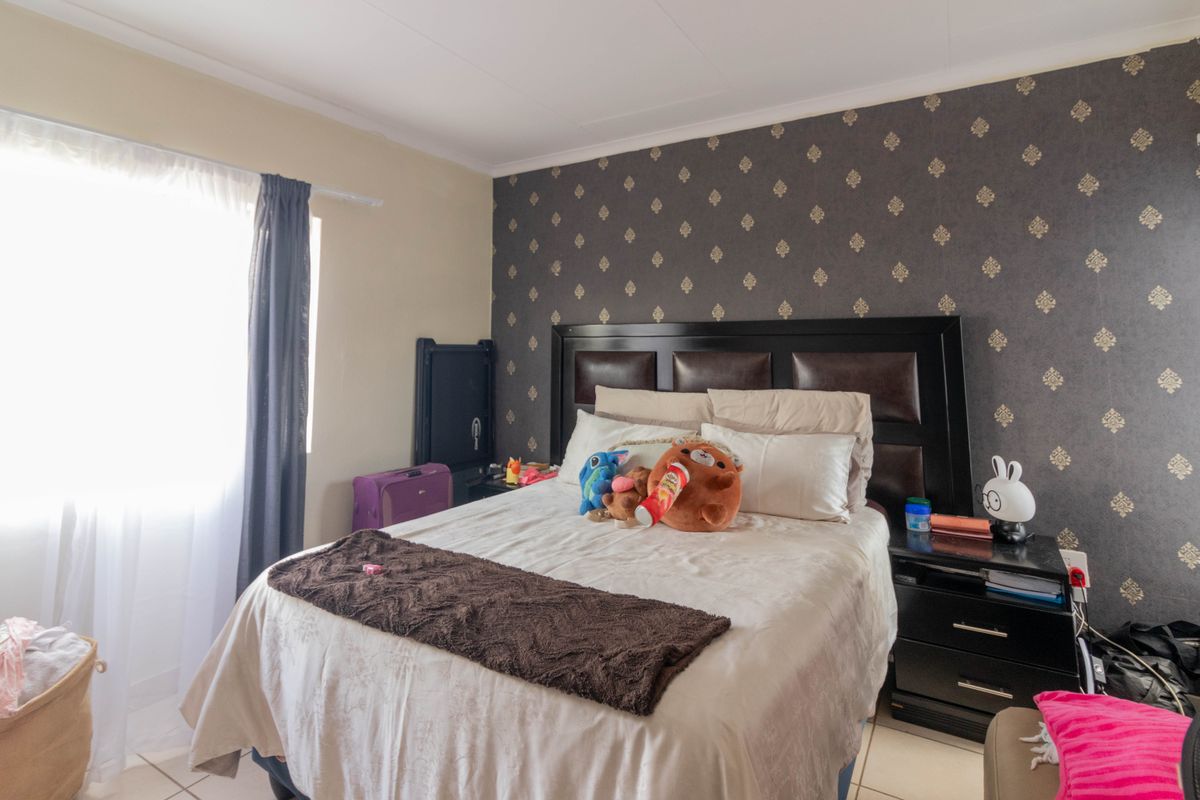 A bedroom featuring a dark patterned accent wall, tiled flooring, and a window with curtains.