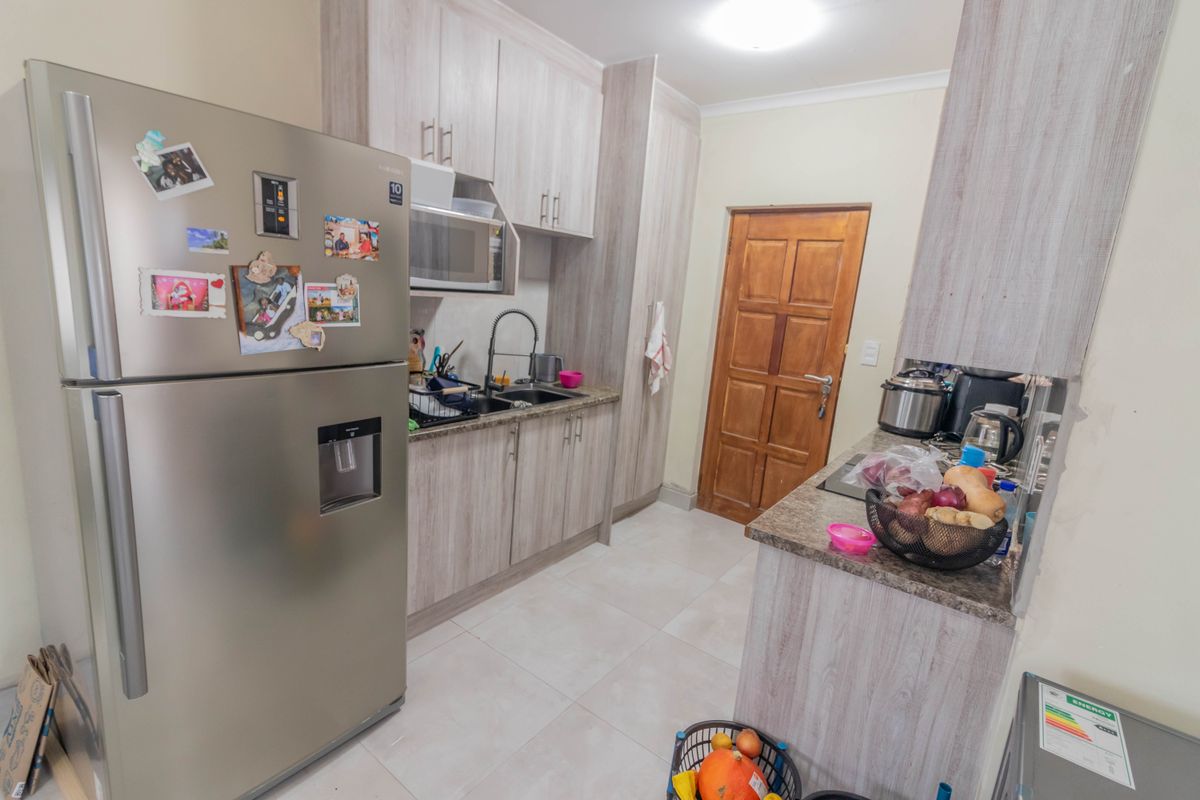 A functional kitchen featuring light wood-grain laminate cabinetry, granite countertops, a double sink with a gooseneck faucet, and tiled flooring.