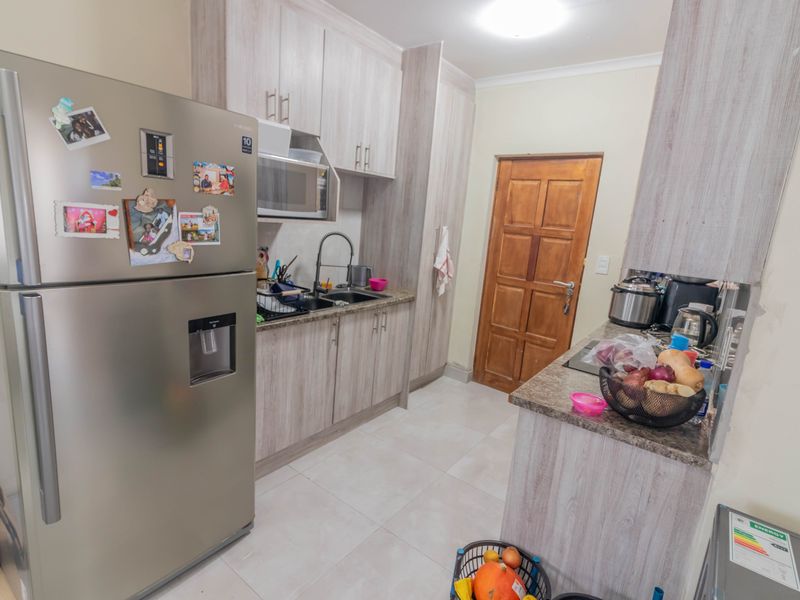 A functional kitchen featuring light wood-grain laminate cabinetry, granite countertops, a double sink with a gooseneck faucet, and tiled flooring.