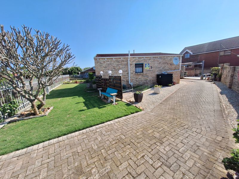A well-maintained rear exterior view featuring brick paving, a neat lawn, and a brick building structure with integrated security and utility features.