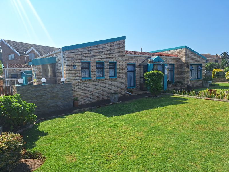 A well-maintained single-story face brick house featuring a landscaped front lawn, paved walkway, and distinctive teal-trimmed window frames.