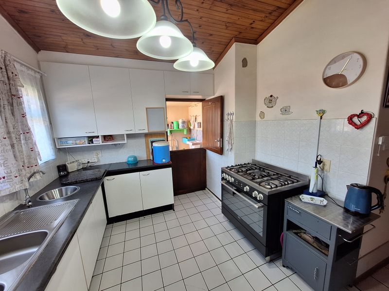 Functional kitchen featuring white cabinetry, gas stove, tiled splashback, and a unique timber ceiling, with direct access to a secondary utility area.