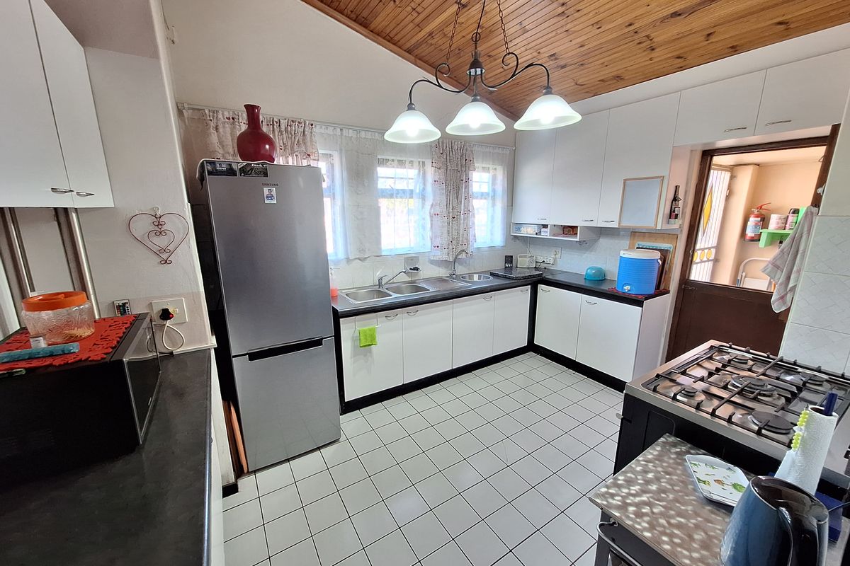 A functional kitchen featuring white cabinetry, a gas hob, double sink, and a distinctive timber-clad ceiling with tiled flooring.