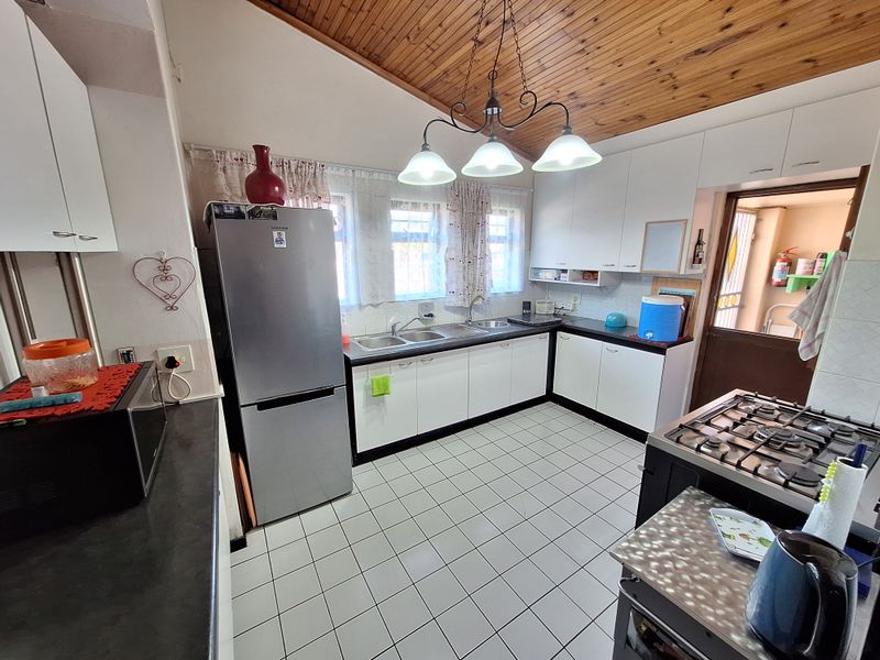 A functional kitchen featuring white cabinetry, a gas hob, double sink, and a distinctive timber-clad ceiling with tiled flooring.