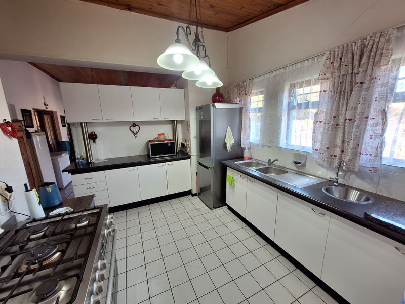 A functional kitchen featuring white cabinetry, tiled flooring, a gas hob, and a timber-paneled ceiling with pendant lighting.