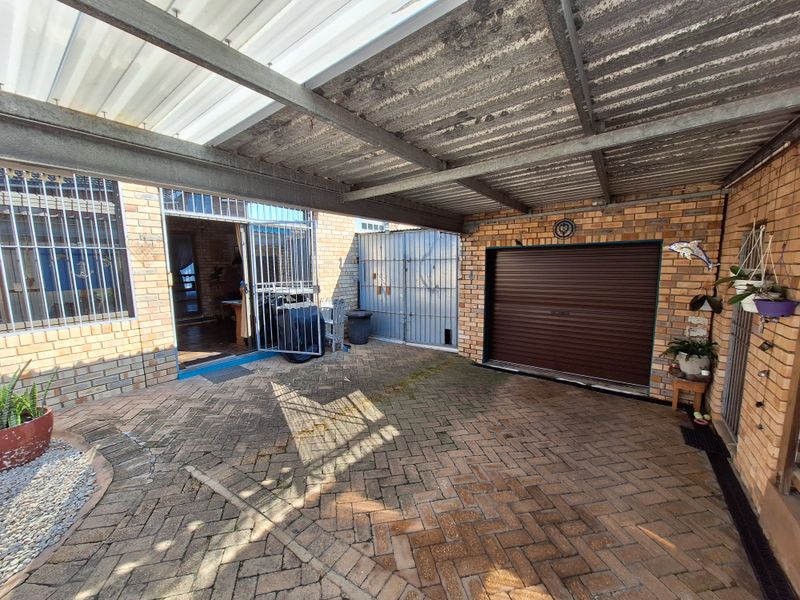 A covered outdoor area featuring brick paving, a roll-up garage door, and a steel-framed roof structure with corrugated sheeting.