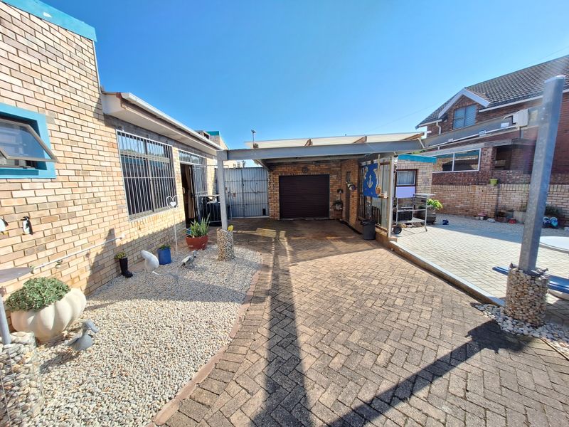 Rear exterior area featuring brick paving, a covered carport, and a garage, providing functional outdoor space and vehicle storage.