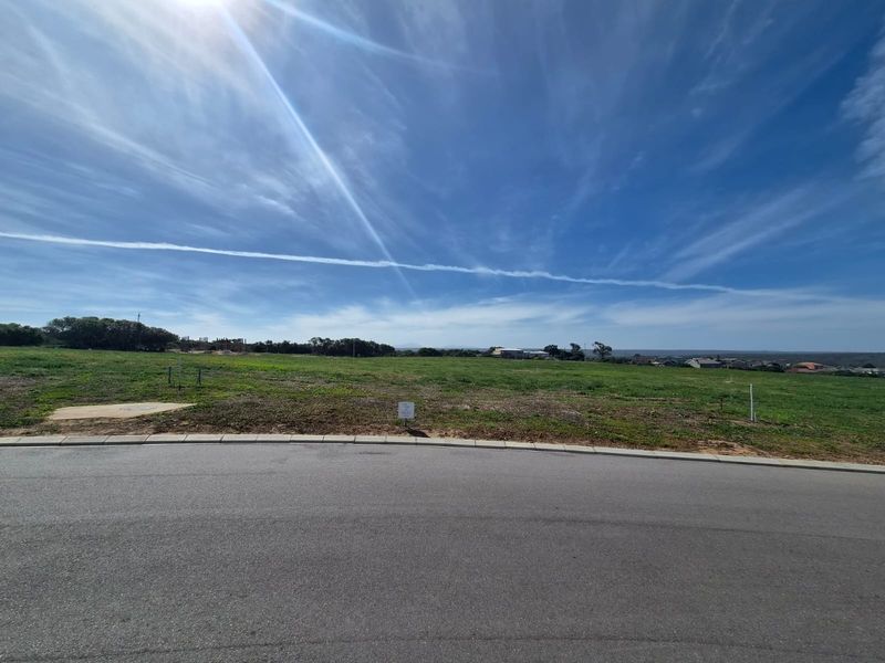 A wide-angle view of a vacant residential plot from the street, featuring level terrain and clear access to the road.