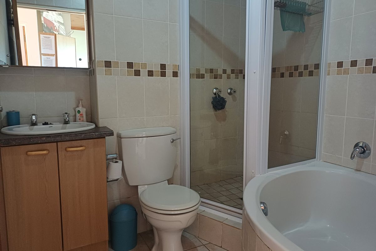 A functional bathroom featuring a corner bathtub, separate shower enclosure, vanity cabinet with basin, and neutral wall tiling.