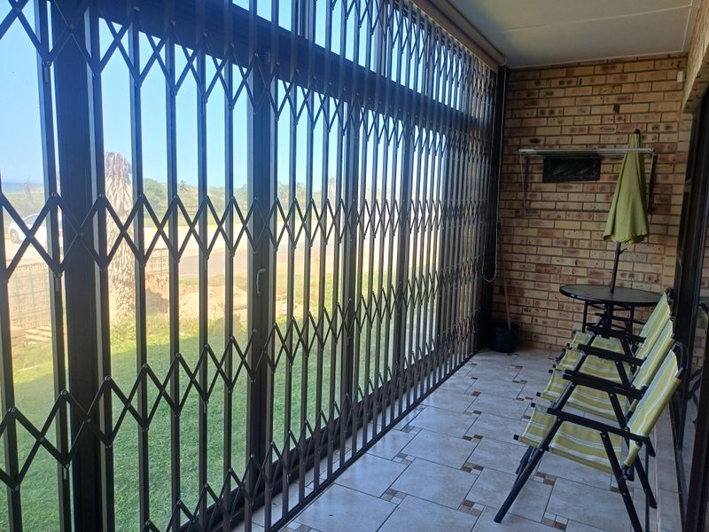 A covered patio area featuring tiled flooring, exposed brick walls, and large sliding glass doors secured with a retractable metal gate.