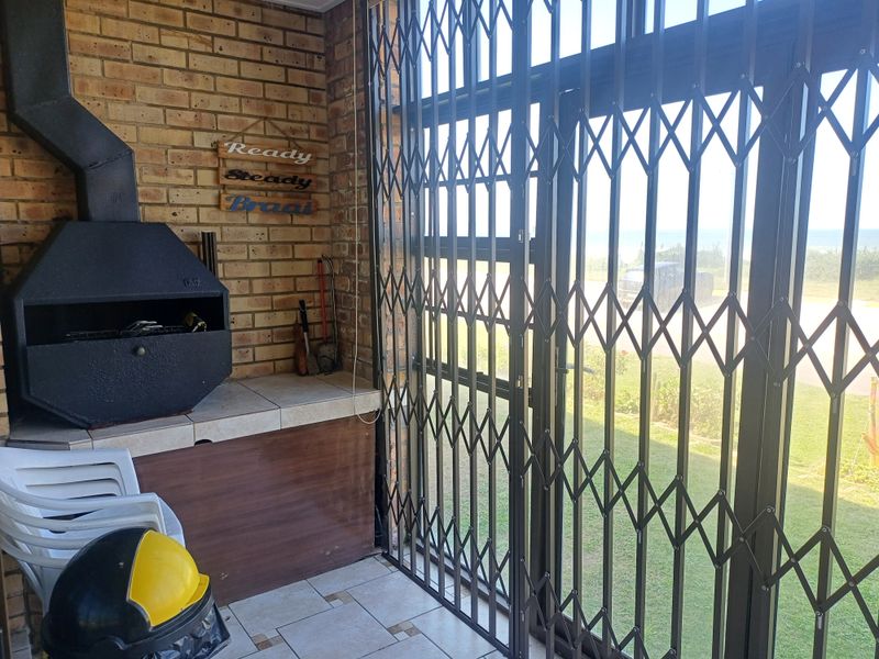 Covered patio area featuring a built-in braai, brick wall finish, and secure metal gate access to the garden.