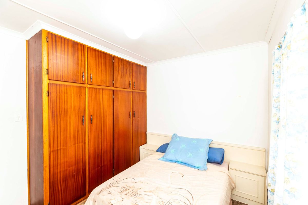 A bedroom featuring a large built-in wooden wardrobe and integrated headboard with matching bedside tables.