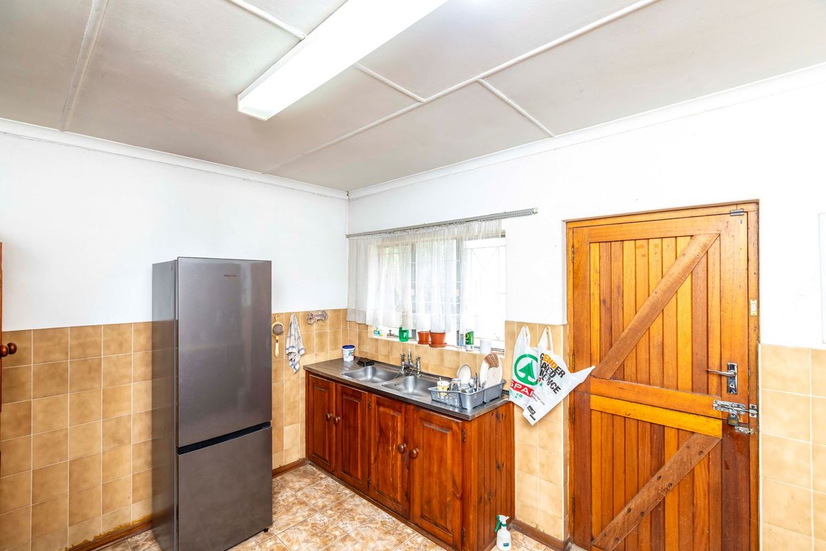 A functional kitchen area featuring wooden cabinetry, a double sink, tiled splashbacks, and a solid wooden door with direct access.