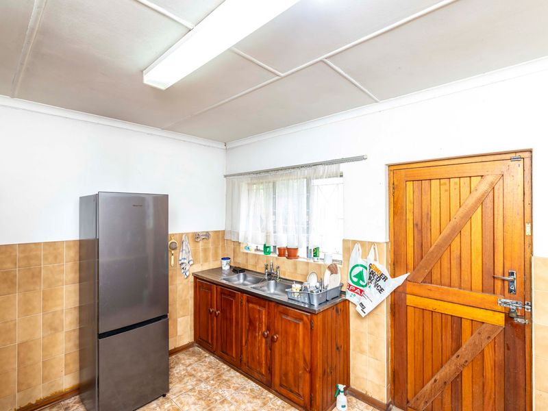 A functional kitchen area featuring wooden cabinetry, a double sink, tiled splashbacks, and a solid wooden door with direct access.