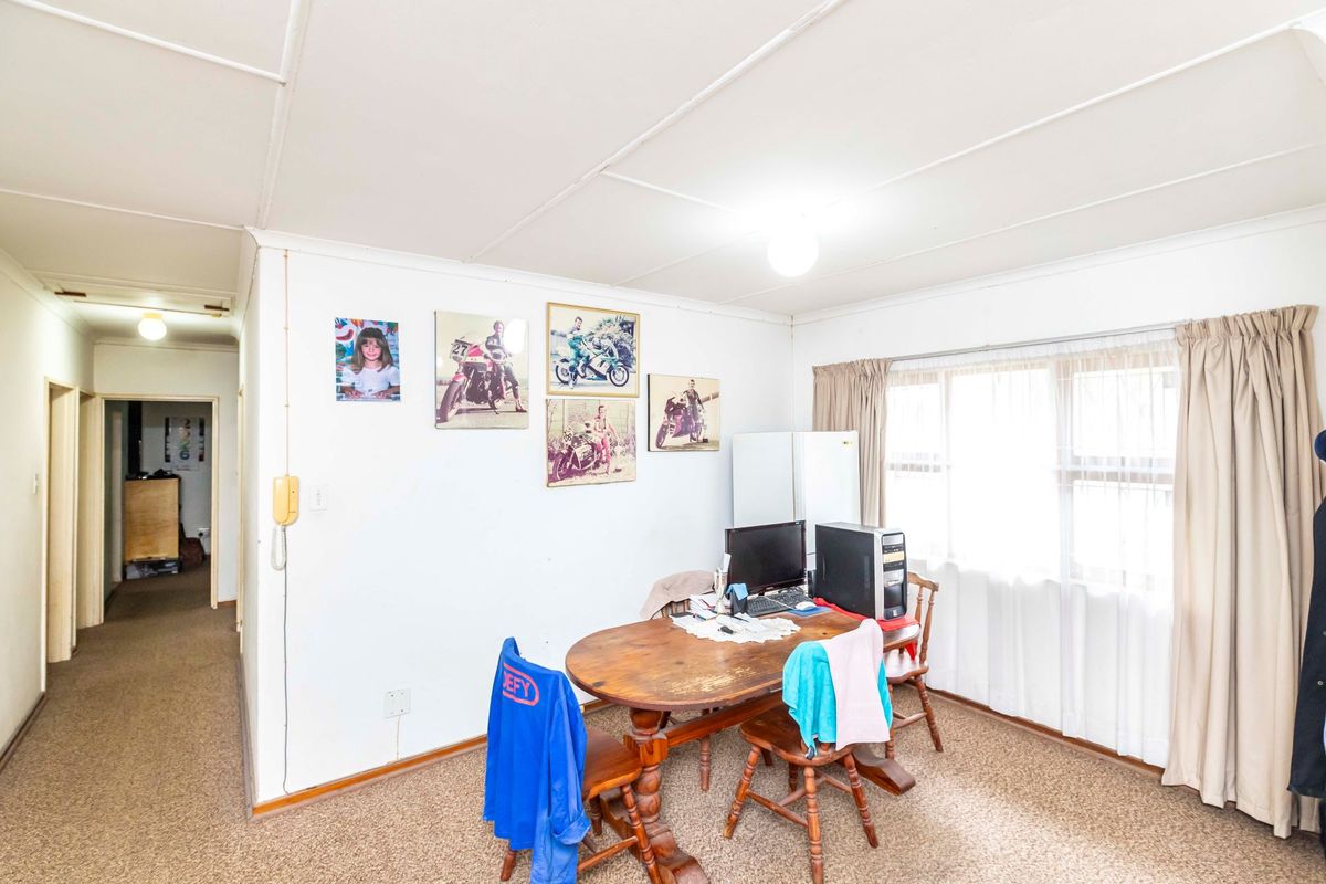 A living area featuring carpeted flooring, a large window with curtains, and a tiled ceiling, offering a functional space with potential for modernization.
