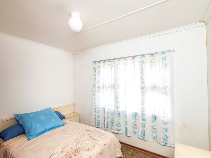 A compact bedroom featuring carpeted flooring, a built-in headboard, and natural light through a window with curtains.