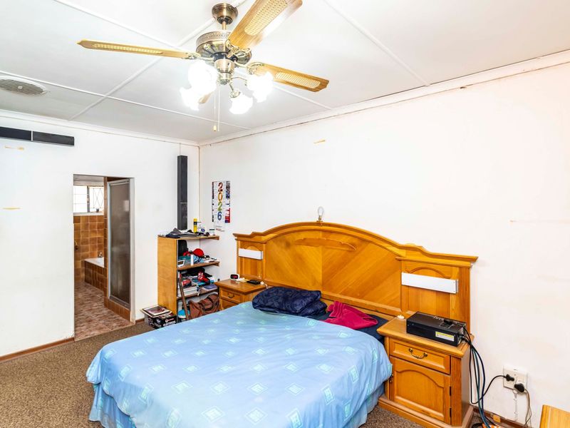 A bedroom featuring a ceiling fan and direct access to an en-suite bathroom, requiring cosmetic updates to the walls and ceiling finishes.